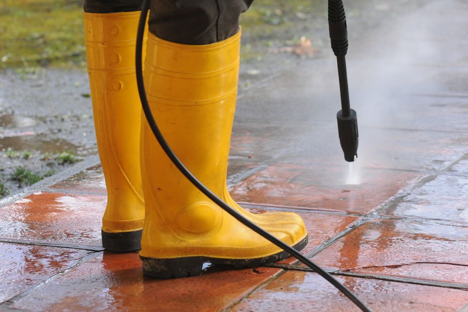 Person Wearing Yellow Rubber Boots With High Pressure Water Nozzle Cleaning The Dirt In The Tiles